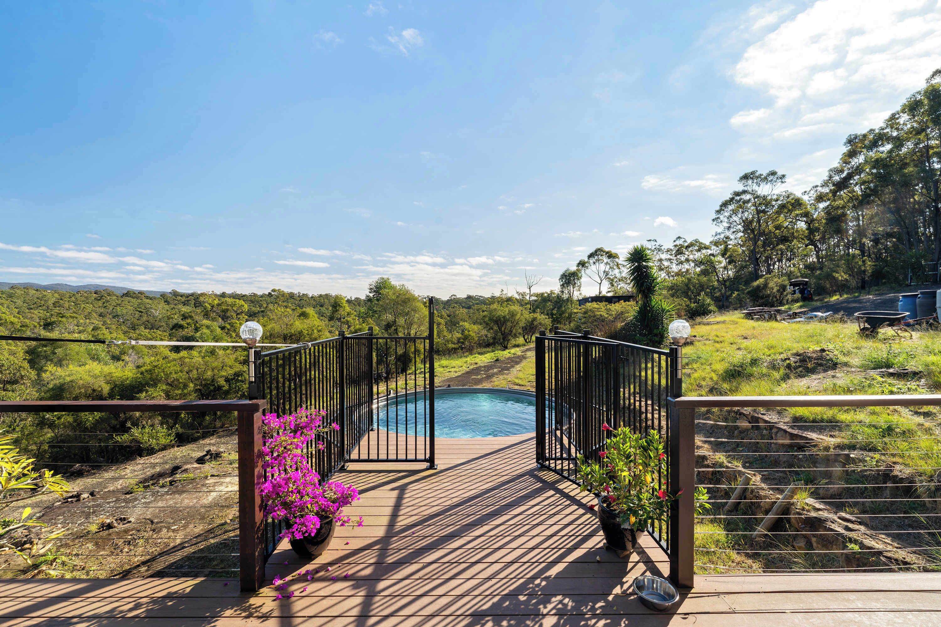 A wooden deck leading to a swimming pool with a view of a forested landscape.