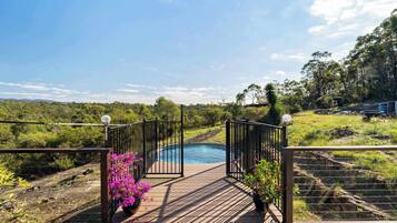 A wooden deck leading to a swimming pool with a view of a forested landscape.