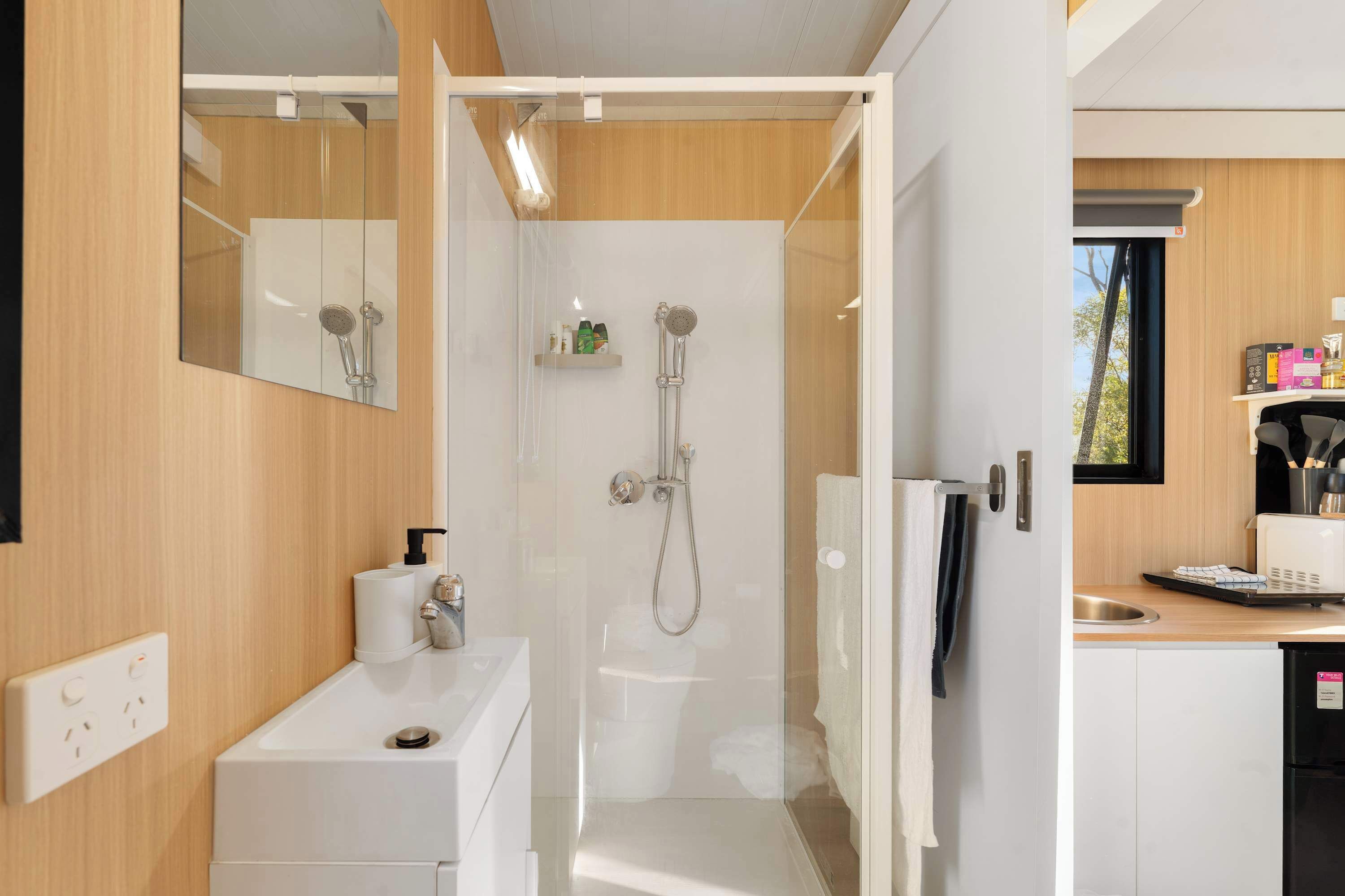 A modern bathroom with a shower, toilet, and sink. There is a mirror above the sink and a window in the shower area.