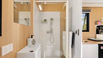 A modern bathroom with a shower, toilet, and sink. There is a mirror above the sink and a window in the shower area.