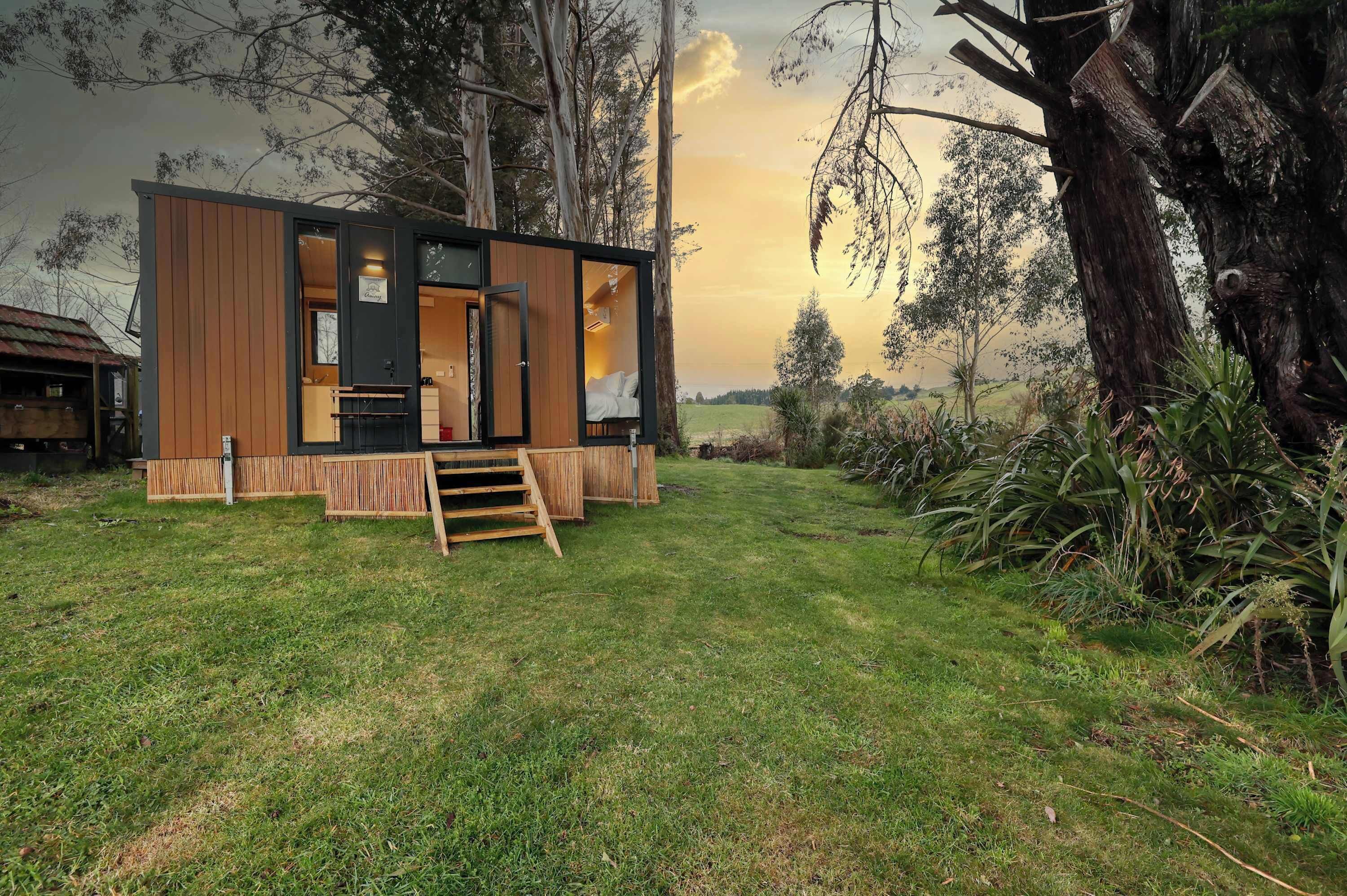 A modern cabin with a wooden exterior, a visible bedroom with a bed, and a small outdoor area with a wooden bench.