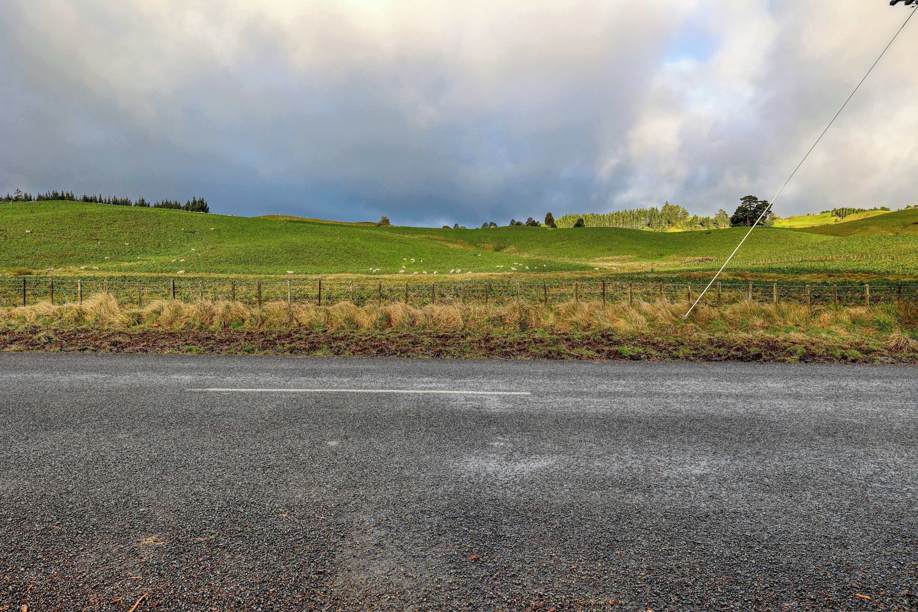 Ländliche Landschaft mit einer Straße, Wiesen und einem Zaun.