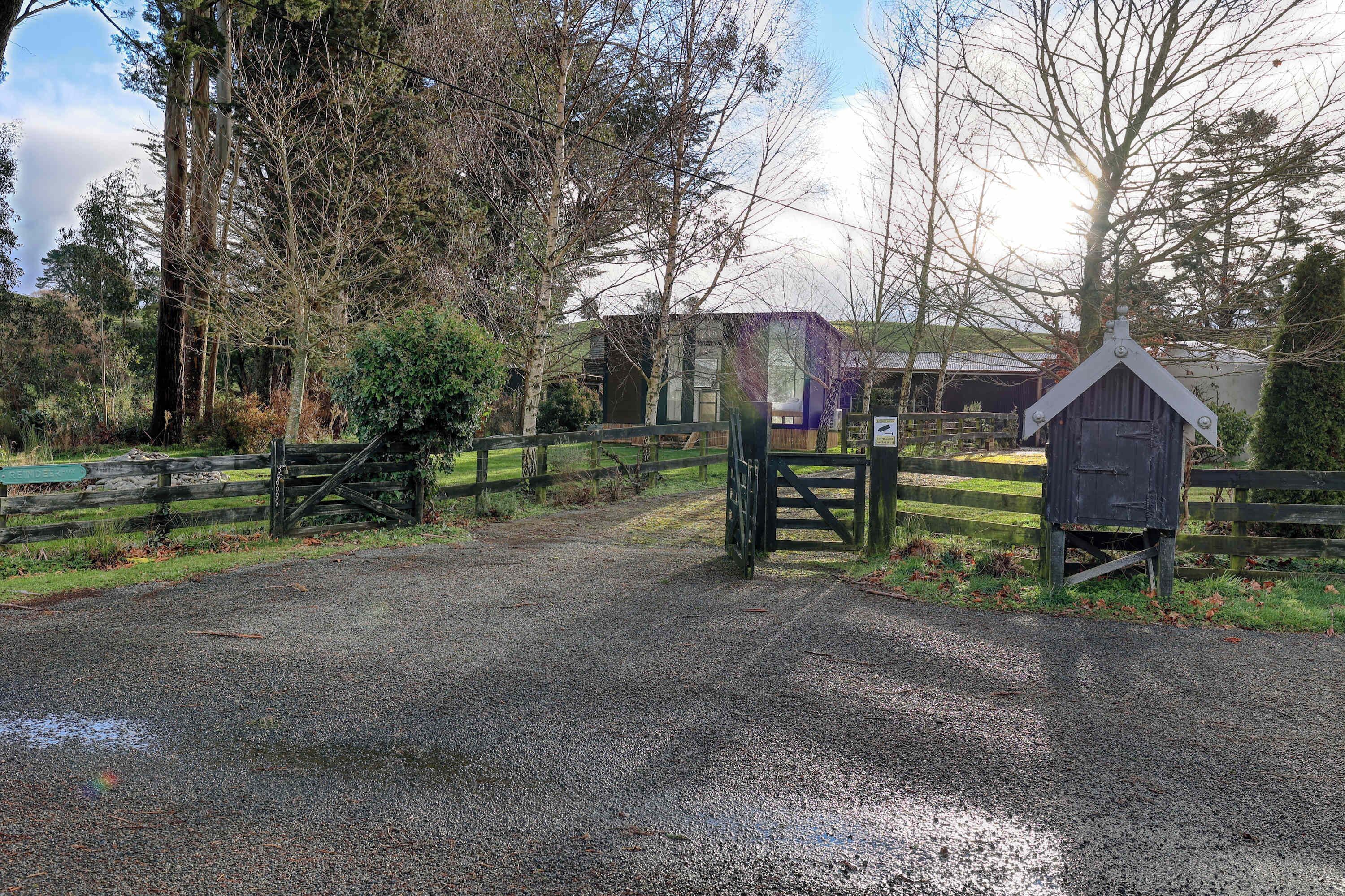 A gravel road leading to a gated area with a wooden gate and a small wooden structure.