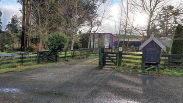 A gravel road leading to a gated area with a wooden gate and a small wooden structure.