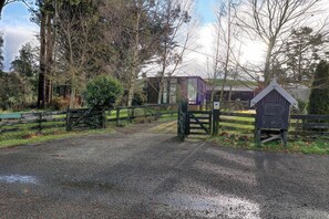 A gravel road leading to a gated area with a wooden gate and a small wooden structure.