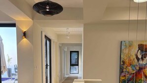 Un interior moderno con un pasillo que conduce a un balcón, un cuadro abstracto grande y una lámpara colgante.