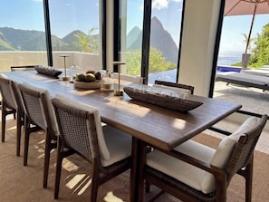 Une table à manger avec des chaises, un saladier de fruits et un verre d’eau.