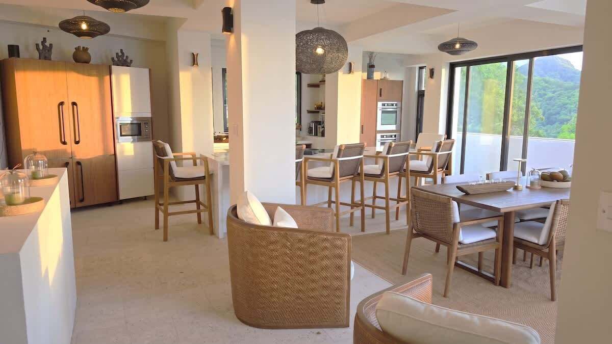 A modern kitchen with built-in appliances, a dining area with wicker chairs, and large windows offering a view of the outdoors.