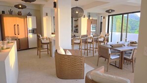 Una cocina moderna con electrodomésticos integrados, un comedor con sillas de mimbre y grandes ventanales con vistas al exterior.
