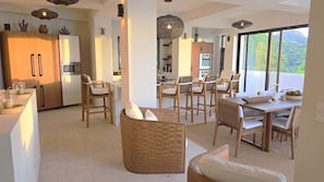 Une cuisine moderne dotée d’appareils électroménagers intégrés, un coin repas avec des chaises en osier et de grandes fenêtres offrant une vue sur l’extérieur.