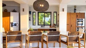 A modern kitchen with a central island, wooden cabinets, and a large window with a view of greenery.