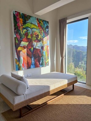 A modern room with a large bed, a colorful abstract painting, and a view of mountains through a large window.