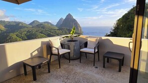 Un balcon offrant une vue sur les montagnes et la mer, avec une table et des chaises.