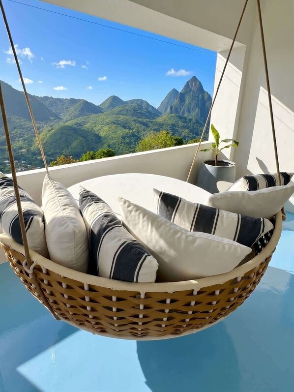A hanging chair with cushions, a potted plant, and a view of mountains.