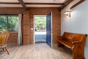Um quarto com um banco de madeira, uma porta que dá para o exterior e uma janela com cortinas.