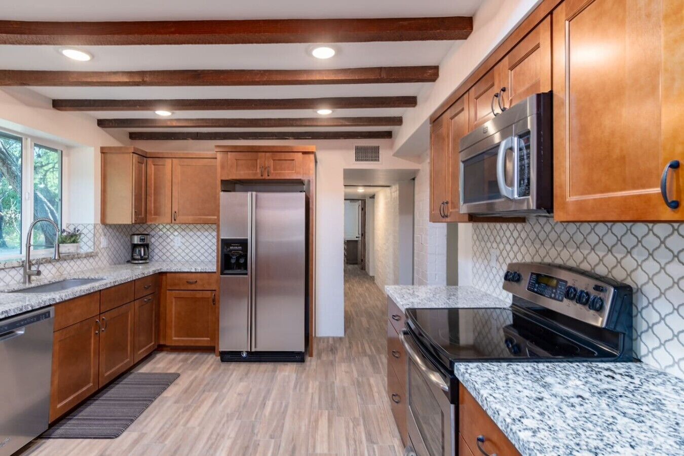 A modern kitchen with wooden cabinets, stainless steel appliances, granite countertops, and a view to the left.
