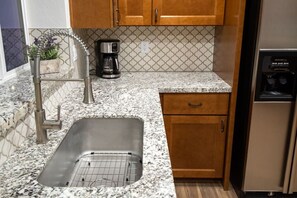 A kitchen with a stainless steel sink, wooden cabinets, a coffee maker, and a refrigerator. - 1945 Ranch House / Tanque Verde / 2 BR 1 BA (Tucson)