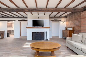 A living room with a fireplace, television, and a round wooden coffee table. - 1945 Ranch House / Tanque Verde / 2 BR 1 BA (Tucson)