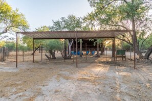 Uma área externa coberta com telhado de metal, rodeada por árvores e uma cerca.