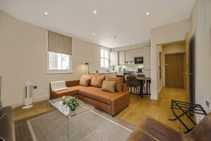 Ein modernes Wohnzimmer mit einer Eckcouch, einem Glastisch und einem Essbereich mit kleinem Tisch und Stühlen.