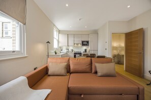 Ein modernes Wohnzimmer mit Sofa, Essbereich und einer Küche im Hintergrund.
