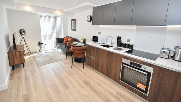A modern kitchen with a built-in oven, a dining area with a table and chairs, and a living room with a sofa and a coffee table. - Modern & Cosy 1 Bedroom Apartment in Leeds (Leeds)