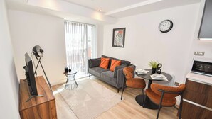 A modern living room with a sofa, dining table, chairs, a TV, and a kitchen area. - Modern & Cosy 1 Bedroom Apartment in Leeds (Leeds)