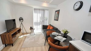 A modern living room with a sofa, a TV, a dining table with chairs, a small side table, and a clock on the wall. - Modern & Cosy 1 Bedroom Apartment in Leeds (Leeds)