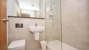 Un bany modern amb vàter, rentapel i plat de dutxa envoltat de vidre.