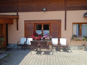 Eine Terrasse im Freien mit Tisch und Stühlen, Holzläden und Blumenkästen.