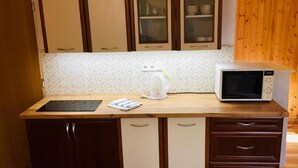 Una cocina con microondas, tetera y un lavamanos pequeño. Se observan armarios de madera y una encimera.