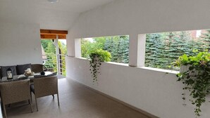 Habitación con comedor, sofá y vistas a árboles a través de amplias ventanas.