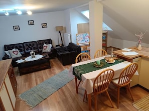 Ein gemütliches Wohnzimmer mit einer Couch, einem Esstisch mit Stühlen, einer Whiteboard-Tafel und einer Lampe.