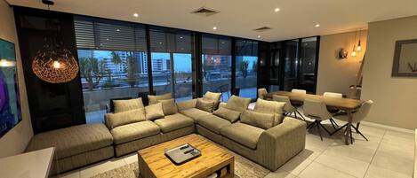 Una sala de estar moderna con un sofá modular, una mesa de centro de madera y una zona de comedor con sillas y una mesa.