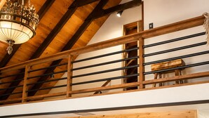 Ein Holzinnenraum mit schrägverdeckter Decke, einer Treppe mit schwarzen Geländern und einem gerahmten Bild an der Wand.