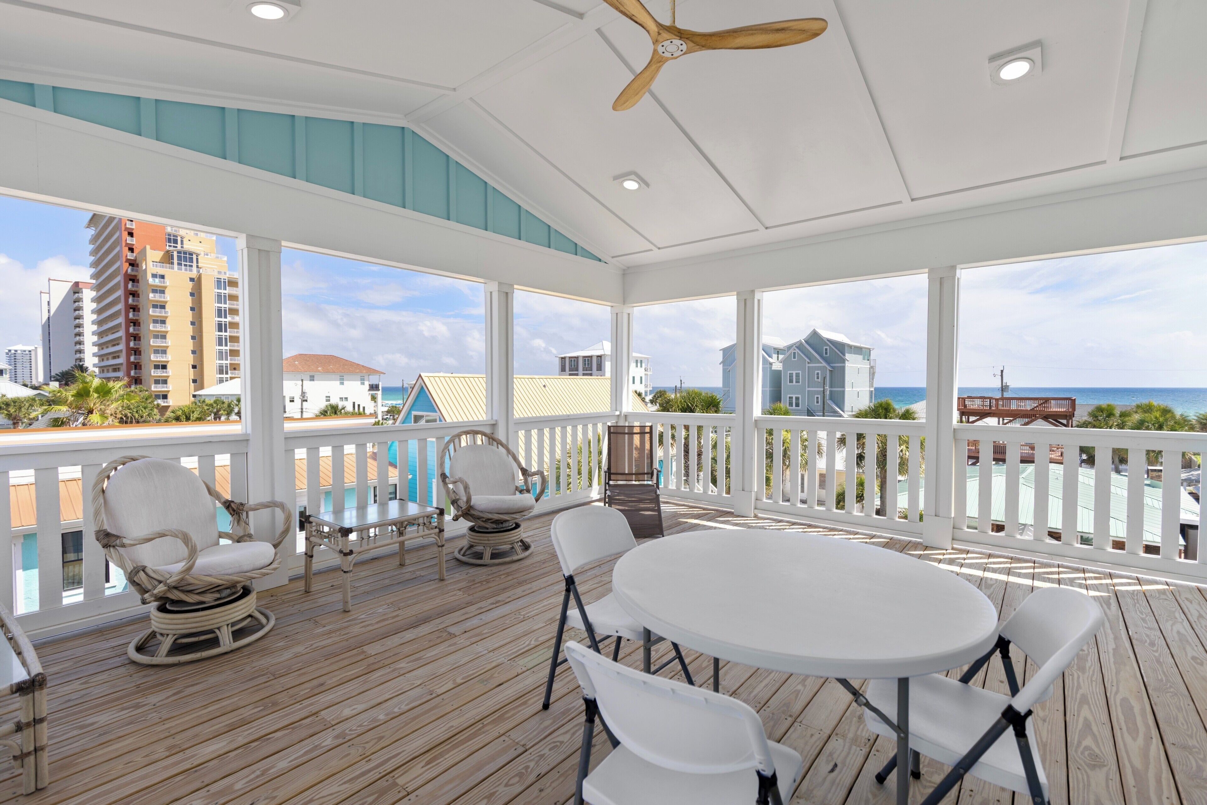 A covered outdoor area with a white ceiling fan, a round table, and white chairs.