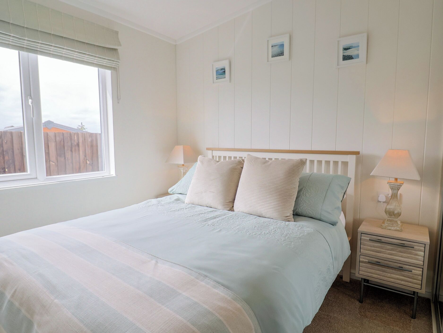 A bedroom with a bed, bedside lamps, a nightstand, and framed pictures on the wall.