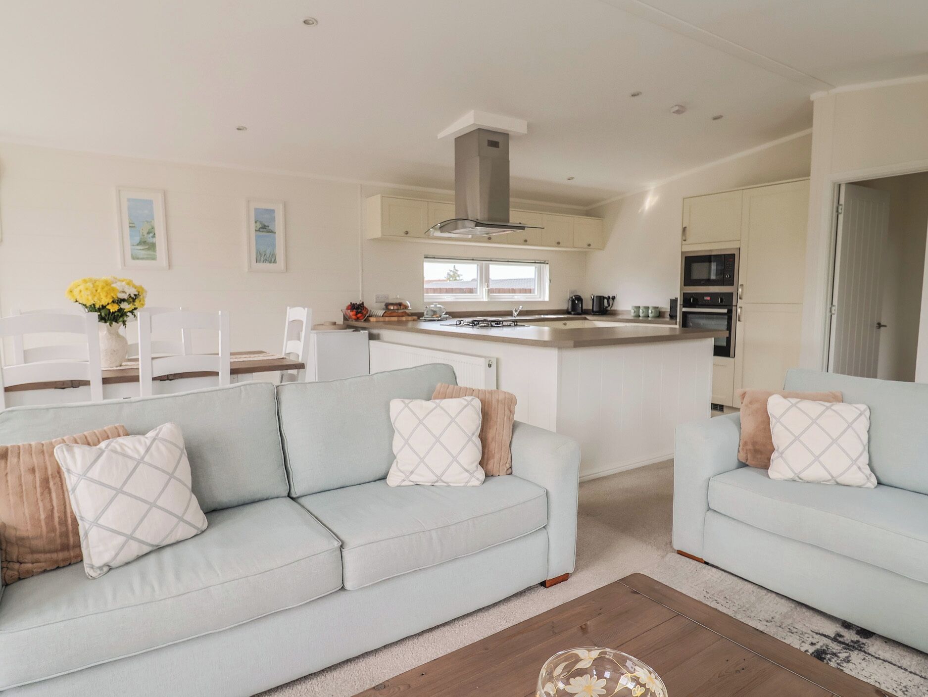 A modern kitchen with a central island, white cabinetry, and a dining area with a white table and chairs.