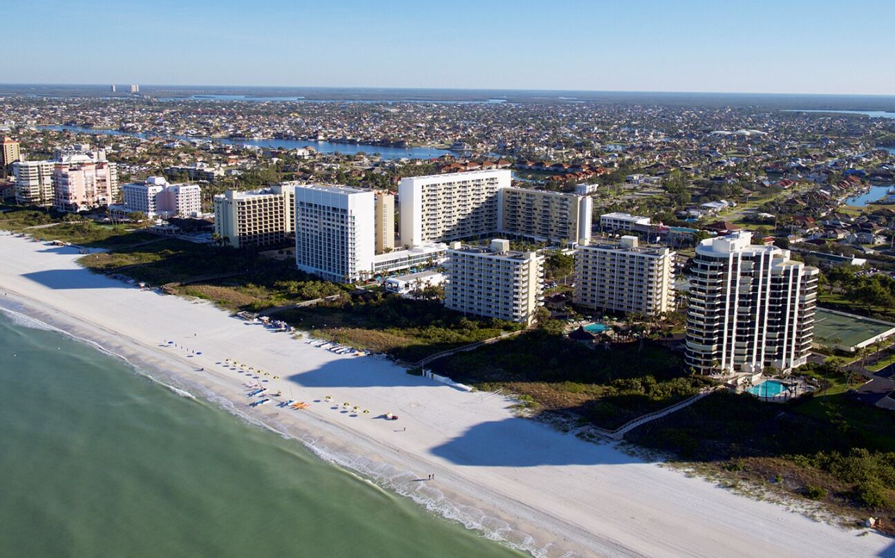 A coastal hotel with multiple high-rise buildings, a beachfront, and a view of the cityscape in the background.