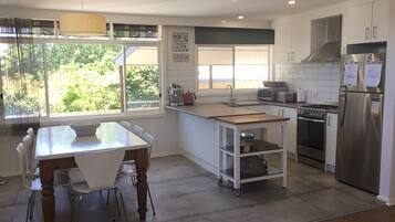 A modern kitchen with a dining table, chairs, a coffee maker, a toaster, a stove, and a refrigerator.