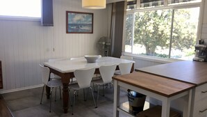 Un'area pranzo con tavolo e sedie, una ventola, una macchina per il caffè e una finestra con vista sugli alberi.