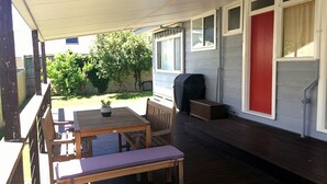 Portico esterno coperto con tavolo e sedie in legno, barbecue e una porta rossa.