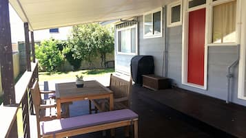 A covered outdoor patio with a wooden table and chairs, a barbecue grill, and a red door.