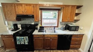 A kitchen with wooden cabinets, a black stove, a sink, a microwave, and a window. - Terrific Scituate Rental ~ 8 min walk to sandhill beach (Scituate)