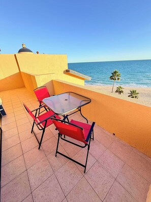 Eine Terrasse mit Tisch und Stühlen, Blick aufs Meer und eine gelbe Wand.