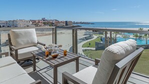 A balcony with a table, two chairs, and a view of the beach and pool area. - Beachfront Paradise 4br/4ba Elegant Condo With Breathtaking Views (Puerto Peñasco)