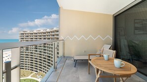 A balcony with a view of a hotel building, a round wooden table with chairs, and a wall with a zigzag pattern. - One 1403b: Beachfront Bliss Studio in Sandy Beach (Puerto Peñasco)