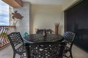 A balcony with a round metal table and chairs, a decorative wall piece, and a view of the beach. - Fully Renovated 1br/1ba Clean Modern Ocean View Condo (Puerto Peñasco)