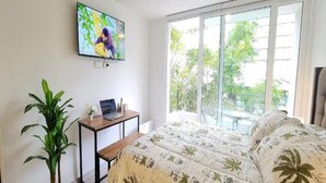 A bedroom with a bed, a TV on the wall, a plant, and a window with a view of greenery. - Rbk Nvo Estudio pasos del Movistar arena (Santiago)