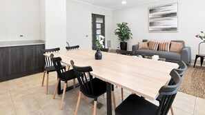 A spacious dining area with a long table and chairs, a sofa, a potted plant, and a wall-mounted artwork.